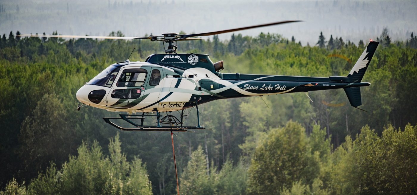 Slave Lake Helicopters' H125 flying over a forest in Alberta, Canada